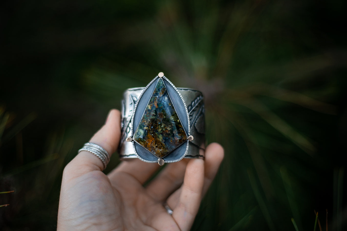 Large kite shaped Moss Agate set in a large sterling silver cuff with recycled 14K gold ball accents being held up by the artist's hand.  